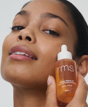 Model holding RMS Kakadu Beauty Oil in a clear bottle with a dropper